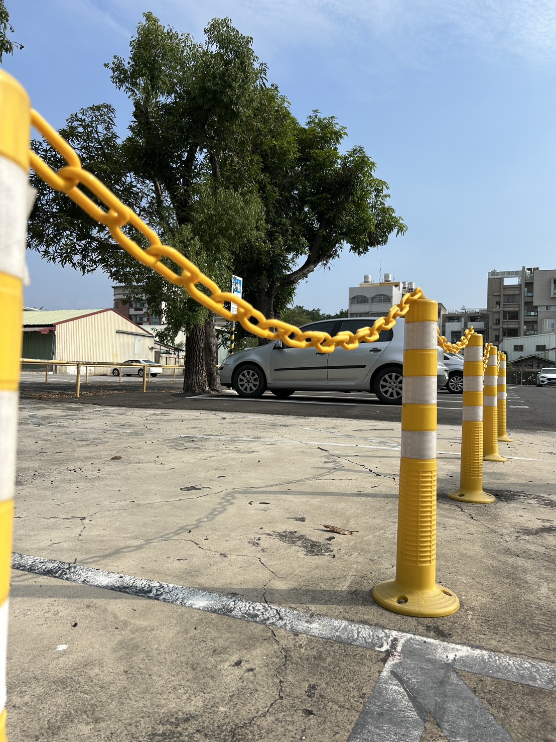 Yellow stanchions connected with a plastic chain used as a barrier in an outdoor parking lot.