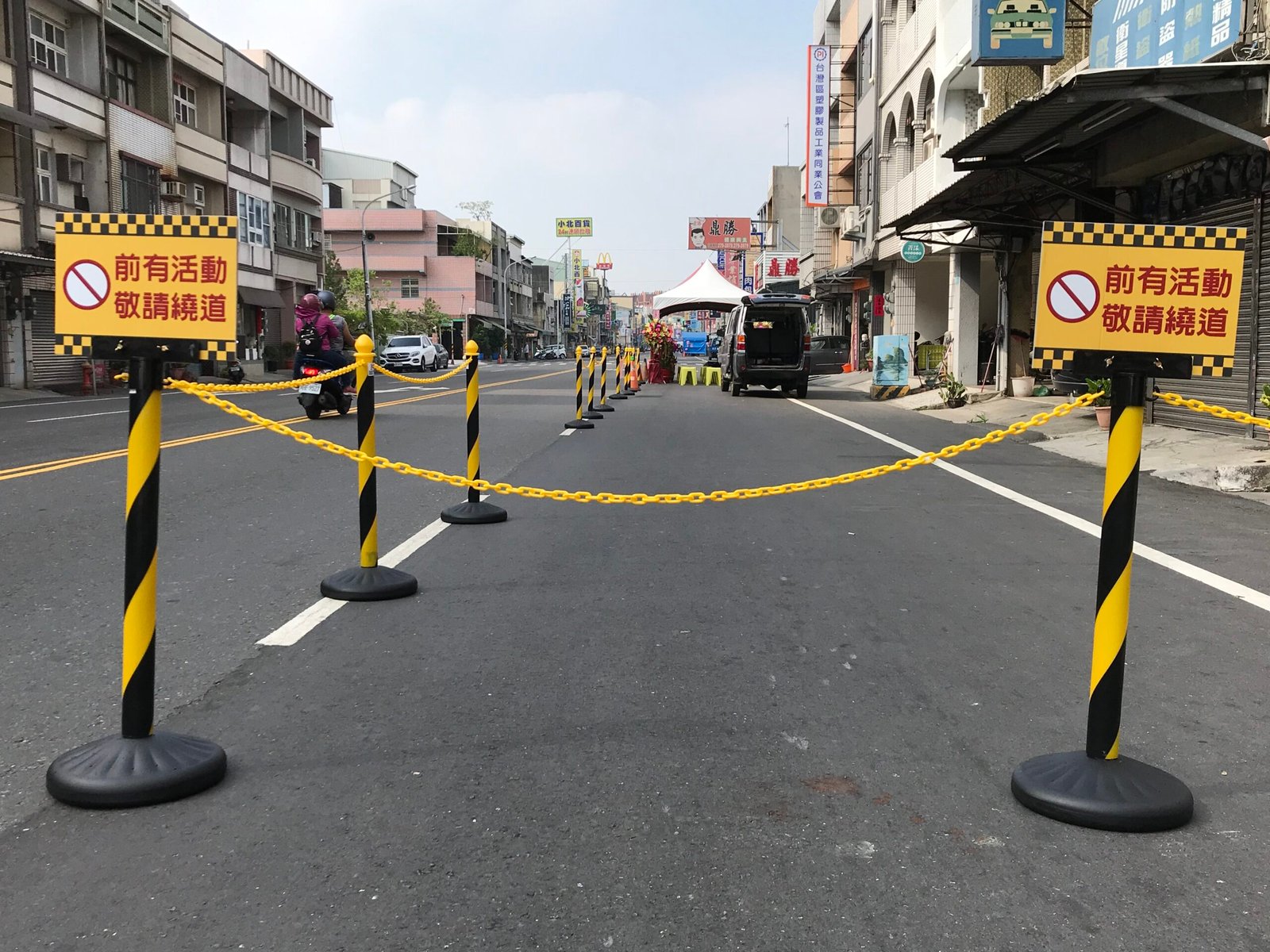 Black-yellow stanchions connected with plastic chains and warning signs used for temporary street closure and traffic control.