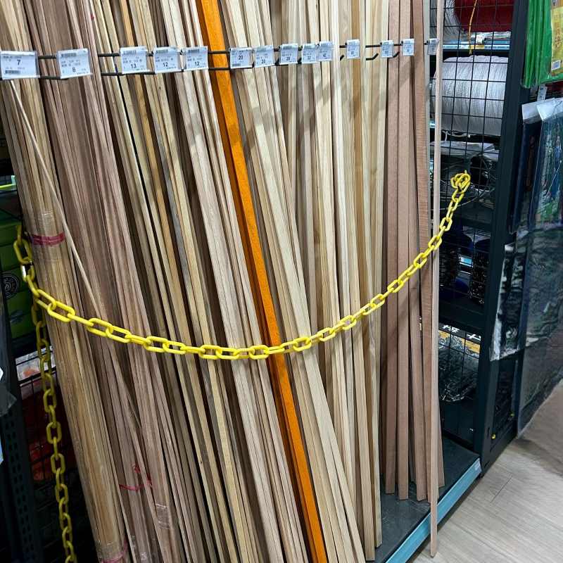 Yellow Plastic Chain used as a barrier in front of stacked wooden planks on a retail hardware store shelf.