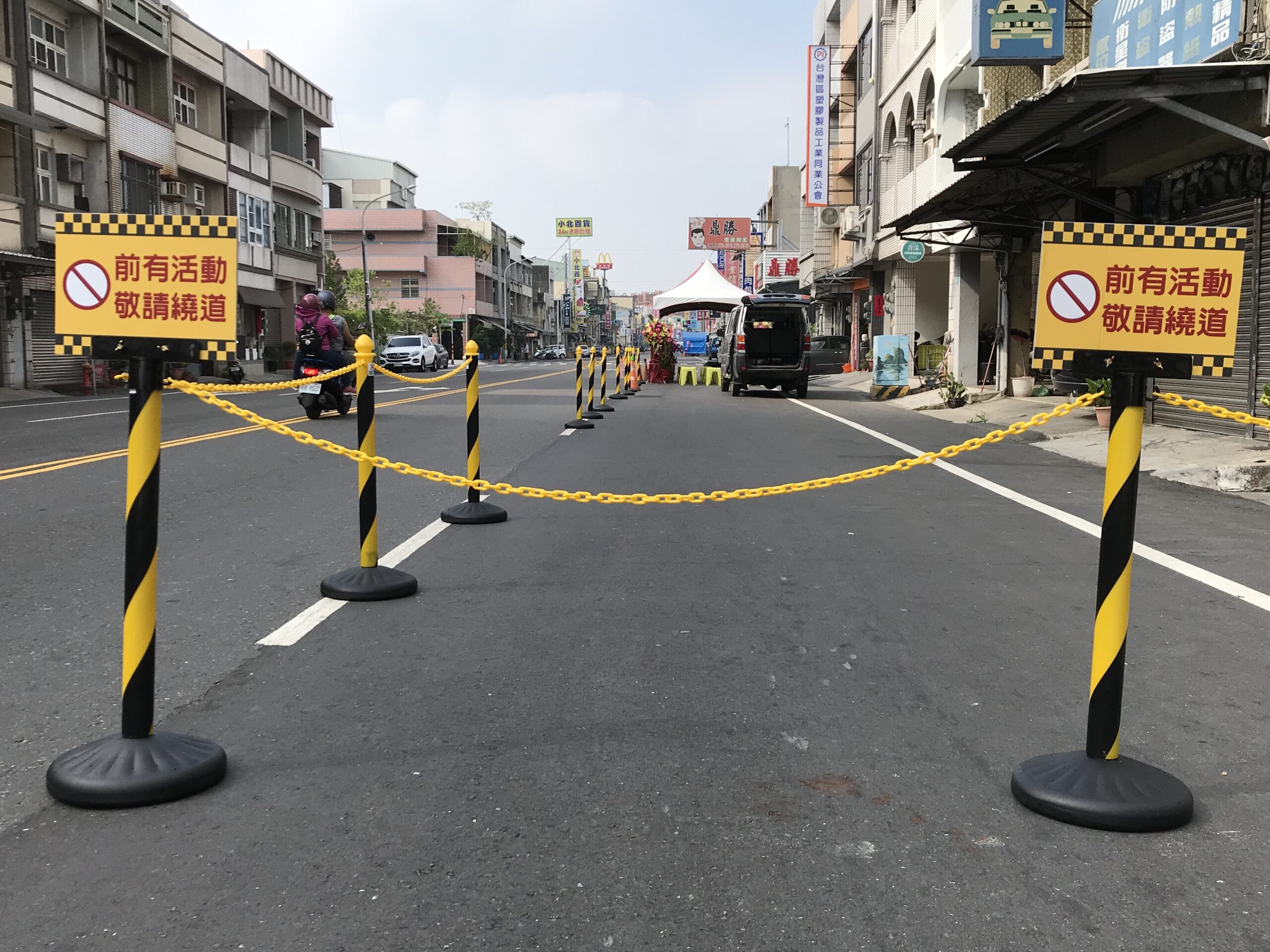 Black-yellow stanchions connected with plastic chains and warning signs used for temporary street closure and traffic control.