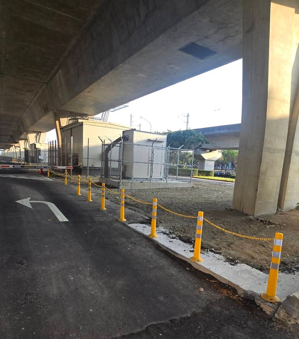 Yellow safety chain connected between reflective posts along an industrial access road beneath an overpass
