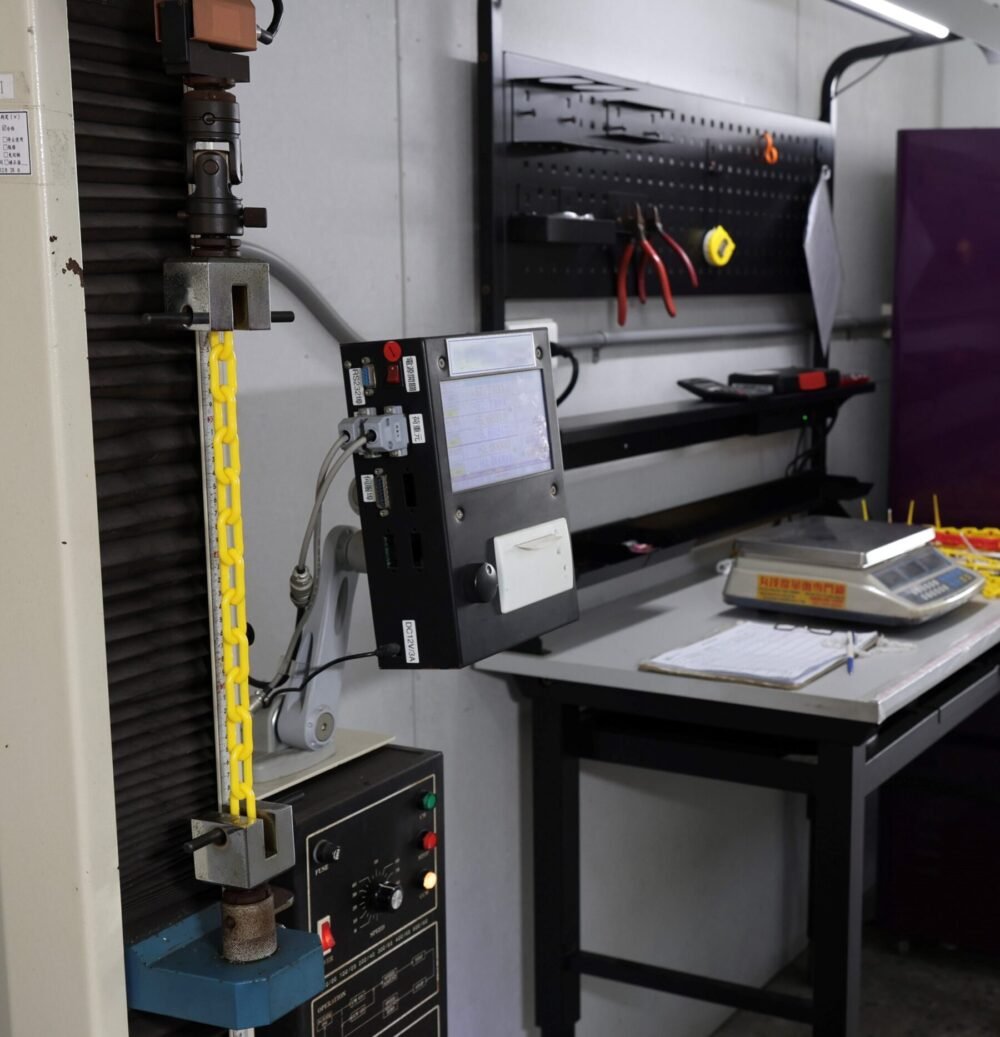 Yellow plastic chain undergoing tensile strength testing in a quality control laboratory.
