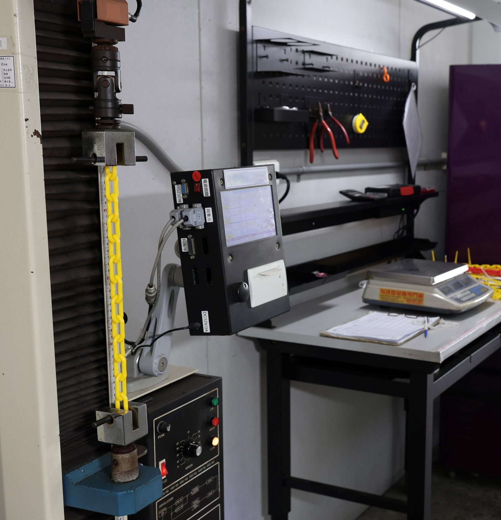 Yellow plastic chain undergoing tensile strength testing in a quality control laboratory.